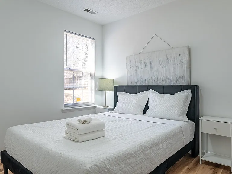 Furnished bedroom with a full/queen bed, nightstands, and a large window with blinds for comfortable everyday living.