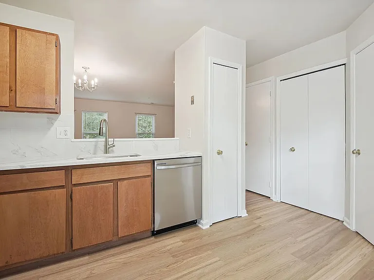 Overview of the kitchen with stainless steel appliances and the doors to the coat closet, pantry, laundry closet, and half-bath. The living area is visible beyond through the pass-through opening and hallway.