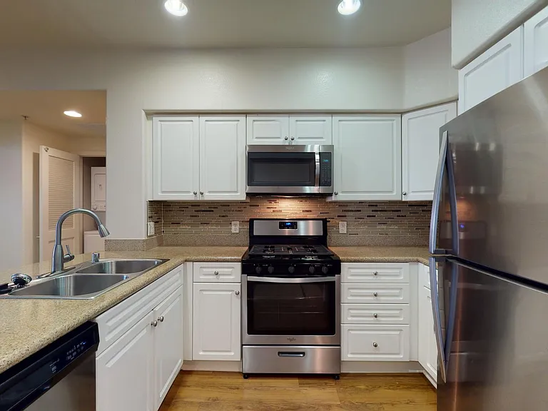 Apartment kitchen with stainless steel appliances, granite countertops, and wood-style flooring.