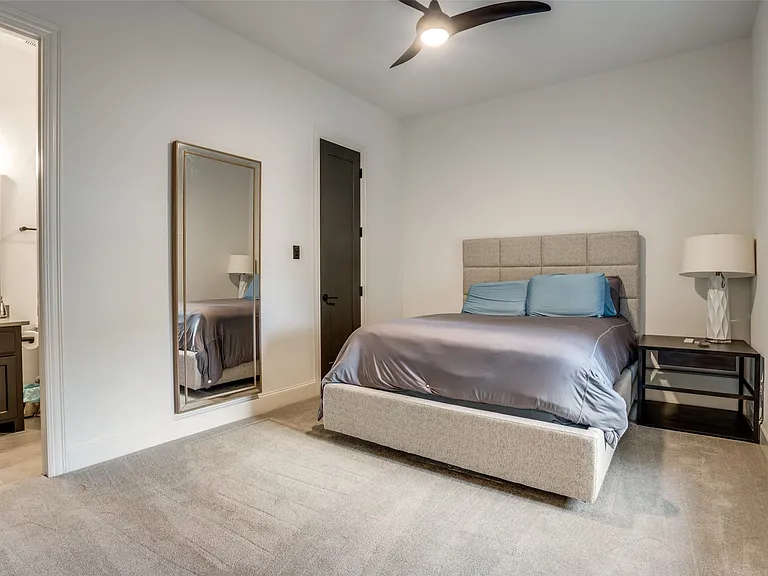 Carpeted bedroom featuring a dark-finish ceiling fan, a dark-finish door with black hardware, and an open doorway revealing a bathroom with a vanity and mirror