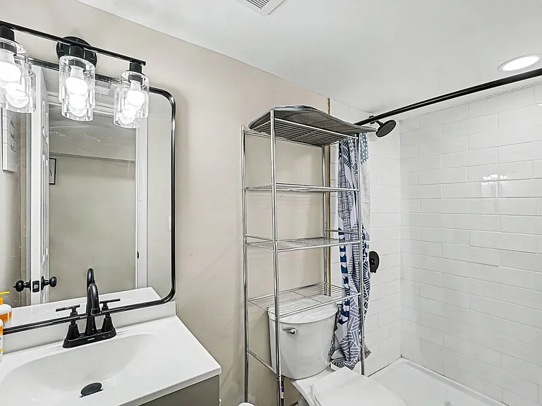 Bathroom with vanity and large mirror, updated light fixture, and tub/shower combo with subway-tile surround.