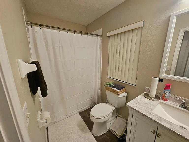 Full bathroom with tub/shower combo, vanity sink with countertop space, and window with blinds for privacy.