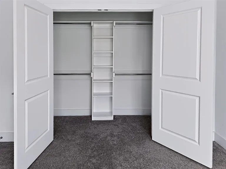 Spacious closet featuring bi-fold panel doors, a built-in shelving unit, dual clothing rods, and soft carpet flooring