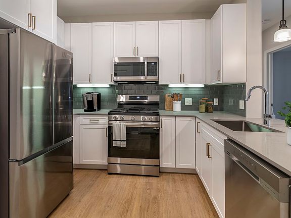 Renovated Package II kitchen with stainless steel appliances, grey quartz countertops, white cabinetry, grey tile backsplash, and hard surface flooring