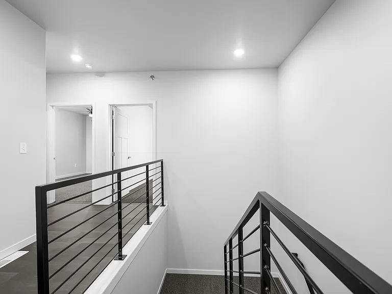 Modern staircase with sleek railing leads to bright hallway with open doors, showcasing a minimalist design. Modern staircase with sleek railing leads to bright hallway with open doors, showcasing a minimalist design.