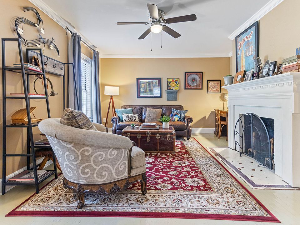 Cozy living room at Hunsucker's Place near Downtown Greensboro, featuring a comfortable leather couch, a functional writing desk, and an open-concept design connecting to the dining room with a piano and the fully equipped kitchen_perfect for relaxation.