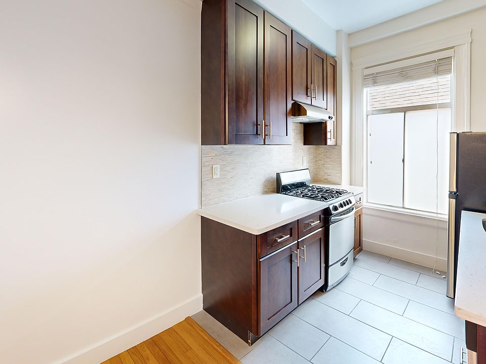 Compact kitchen with wood cabinets, a stainless steel oven, and light countertops. A large window brightens the tiled floor space.