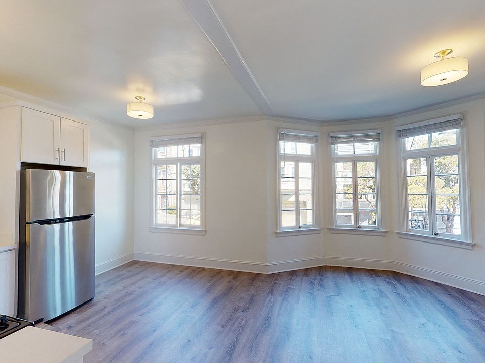Spacious living room with wood-like floors, large windows, and a view of the kitchen