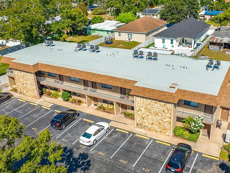 Aerial view of a charming two-story apartment building with ample parking and lush green surroundings.