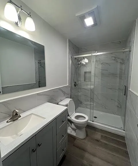 New bathroom with cabinet vanity, new toilet, walk-in shower with sliding glass door