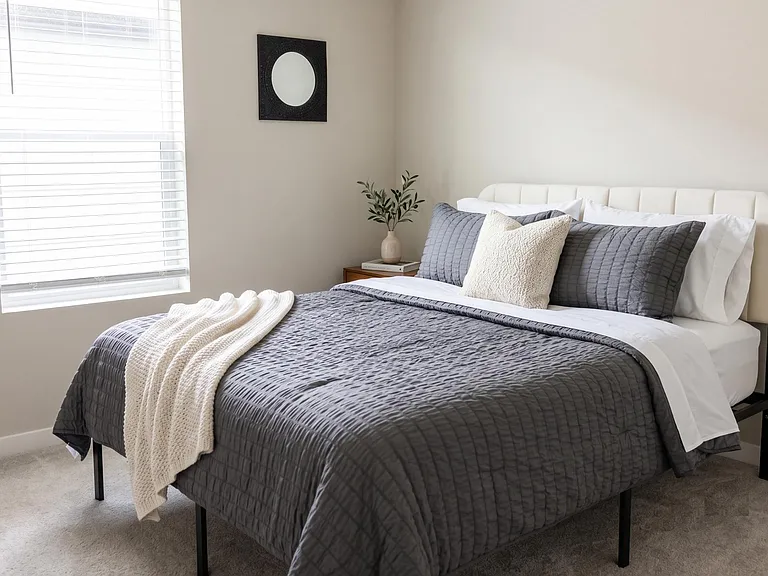 Well-appointed bedroom with a full bed, nightstand, and a large window with blinds for natural light and privacy.