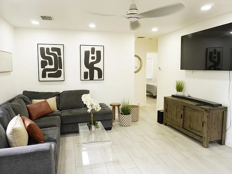 Spacious living area with a sectional, wall-mounted TV, ceiling fan, and tile flooringideal for relaxing or hosting.