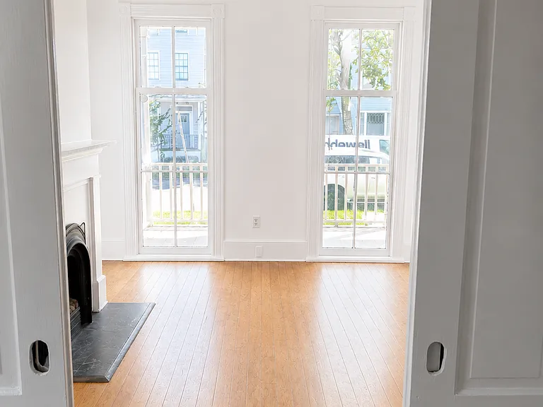 Rendering of front room with white walls and refinished hardwood floors. Looking in from parlor doors