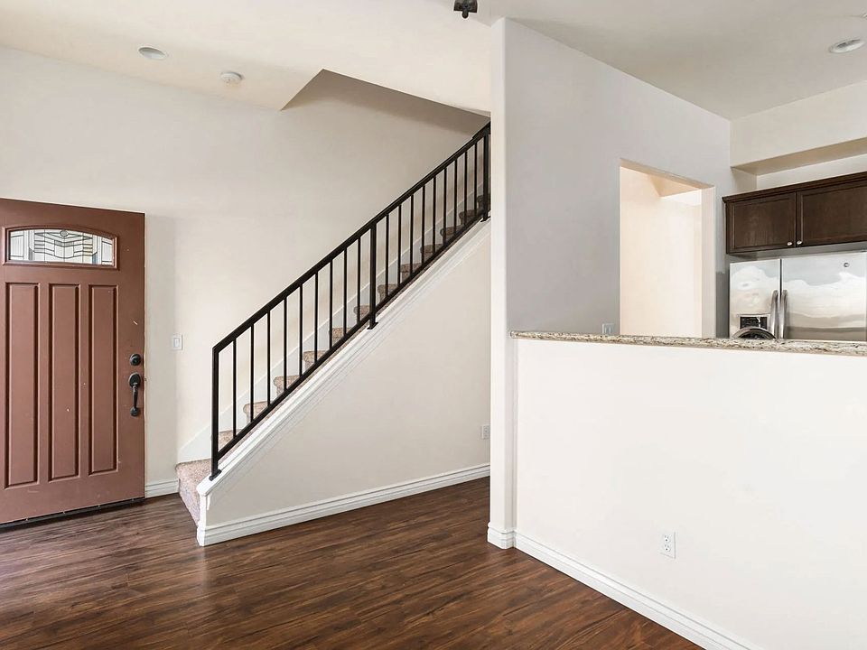 Front entrance with wood style laminate flooring and view of open kitchen with dark wood cabinetry at The Nines Townhomes in Escondido, California.