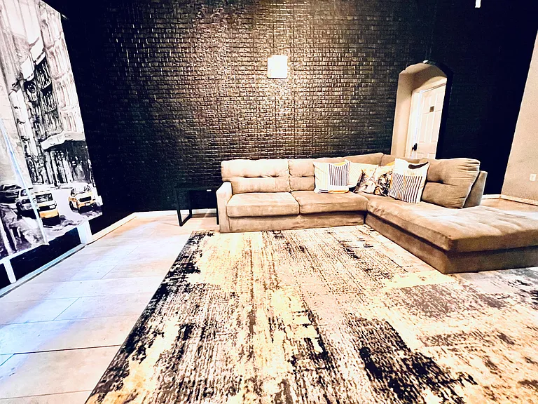 Spacious living area with a large sectional, textured accent wall, and ample floor space for relaxing or entertaining.