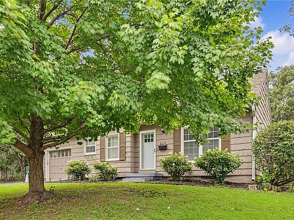 Split-level residence featuring a prominent mature tree, a single garage door, and a light-colored entry door with side windows
