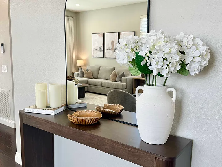 An elegant entry console with a sleek design is paired with a wall-mounted mirror above, creating a stylish focal point. The console features a small dish to conveniently hold keys & other small essentials, keeping the space organized.
