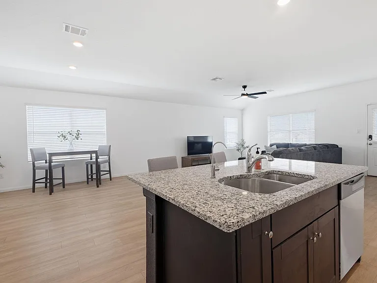 Open-concept kitchen and living area with a granite island, double sink, and space for dining and lounging.