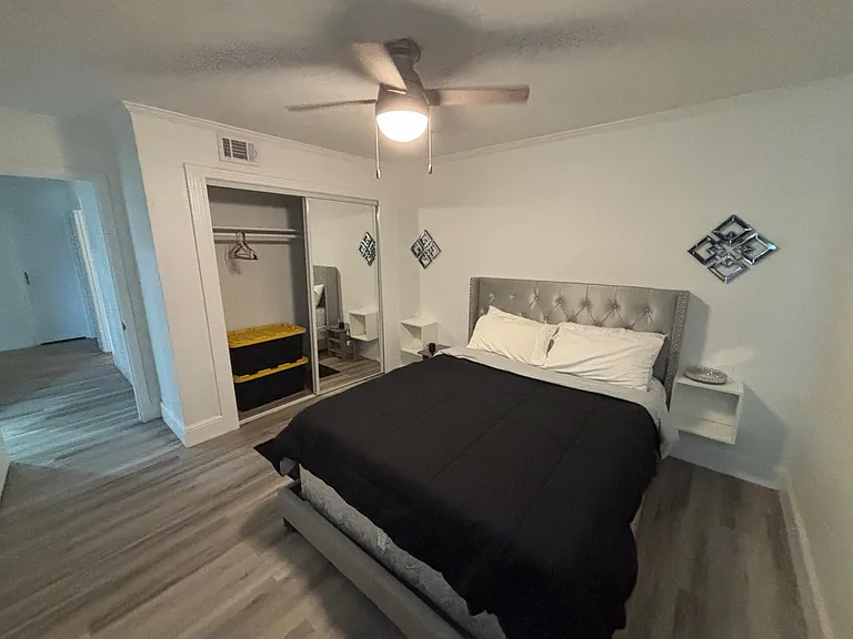 Private bedroom with a full bed, ceiling fan, and nightstands, plus mirrored sliding closet doors for storage.