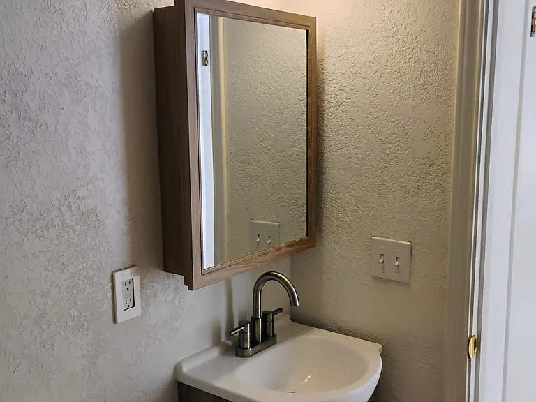 View from inside bathroom showing new vanity, medicine cabinet and light fixture. Toilet is also new