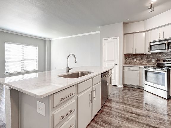Kitchen with island, white cabinets, gray wood-style flooring, and gray backsplash