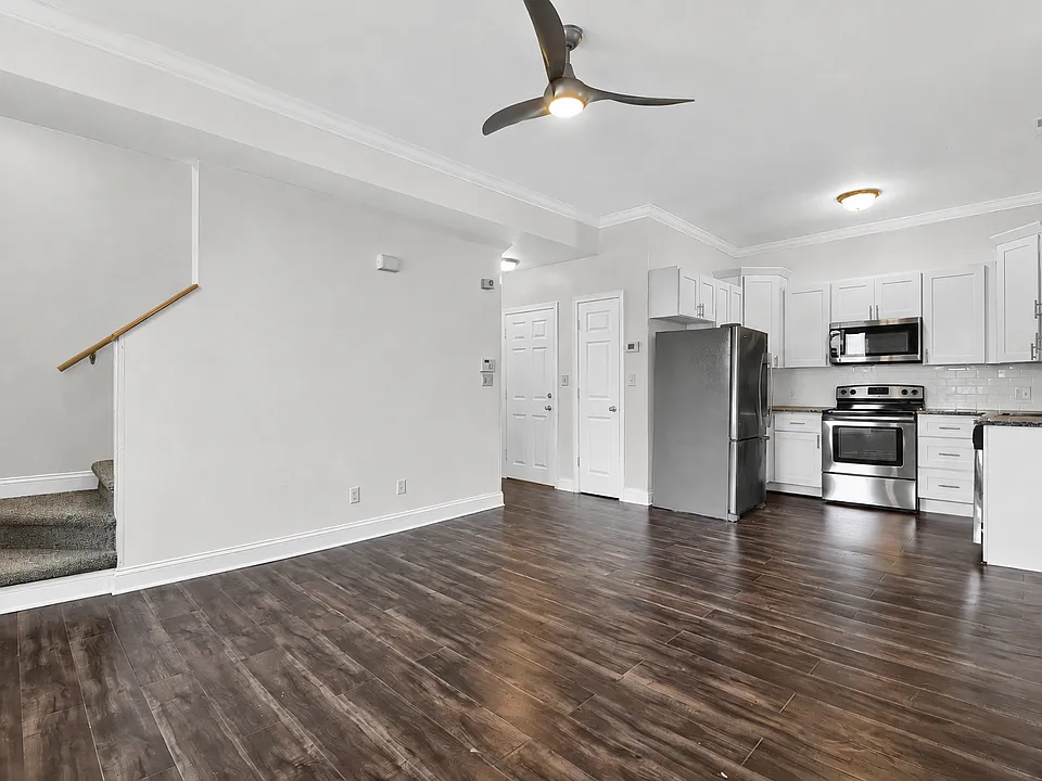 Open first-floor layout connects a family room with 10-foot ceilings to the adjoining kitchen, complemented by wood-style flooring, crown molding, and a ceiling fan.