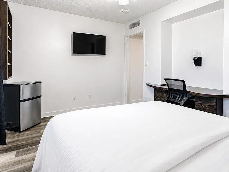 Furnished bedroom with a mounted TV, work desk, and in-room mini fridge for added convenience.