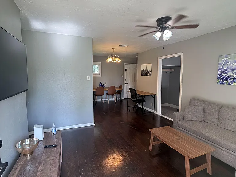 Open living area with hardwood floors, ceiling fan, and space for lounge seating plus a desk and small dining setup.
