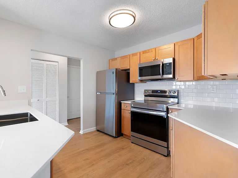 Renovated Package I kitchen with stainless steel appliances, white quartz countertops, maple cabinetry, white tile backsplash, and hard surface flooring