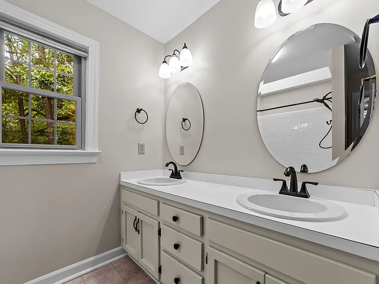 Primary bath with dual vanity, round mirrors, black fixtures, and natural light.