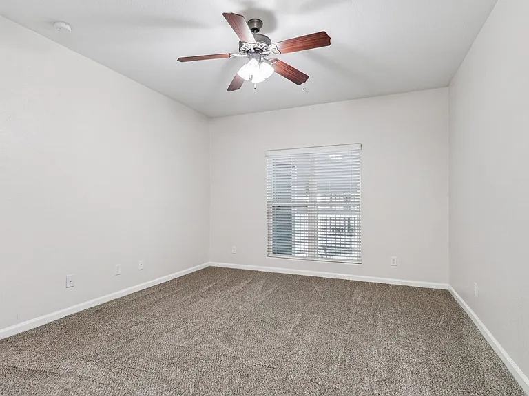 Spacious bedroom with plush carpet and ceiling fan, featuring large window for natural light. Spacious bedroom with plush carpet and ceiling fan, featuring large window for natural light.