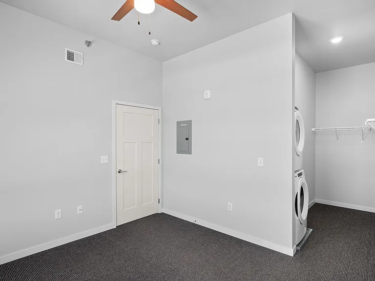 Modern room with sleek built-in laundry area, featuring a stacked washer and dryer alongside a spacious carpeted area. Modern room with sleek built-in laundry area, featuring a stacked washer and dryer alongside a spacious carpeted area.