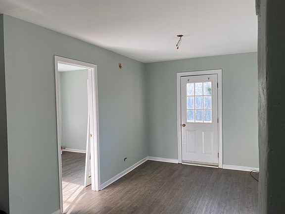 Newly painted living area with open door to bedroom and closed door to the porch. Flooring is new. Ceiling fan to be installed.