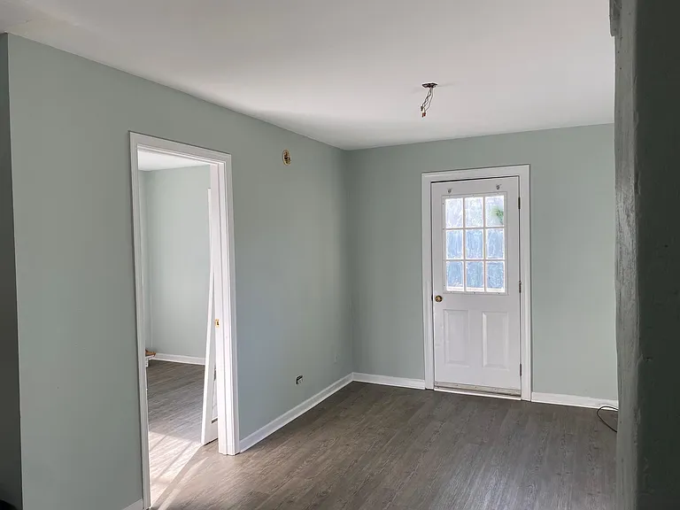 Newly painted living area with open door to bedroom and closed door to the porch. Flooring is new. Ceiling fan to be installed.