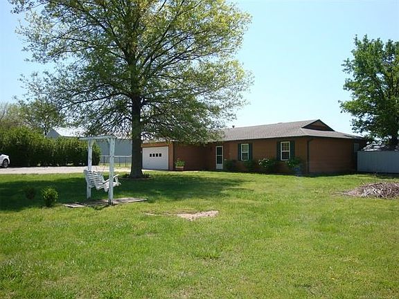 View of NW corner of house with several mature shade trees & privacy hedges near parking area.