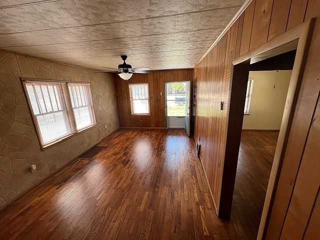 View of living room, from brick partial wall. Opening into interior hallway is on the right, with 1st bedroom partially visible.