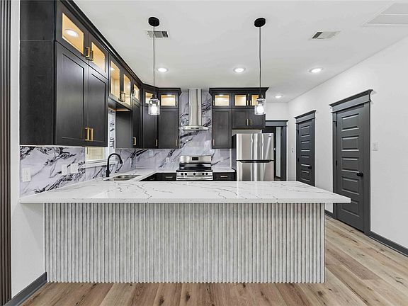 Updated kitchen with large waterfall peninsula, stainless appliances, and ample cabinet storage with statement tile backsplas