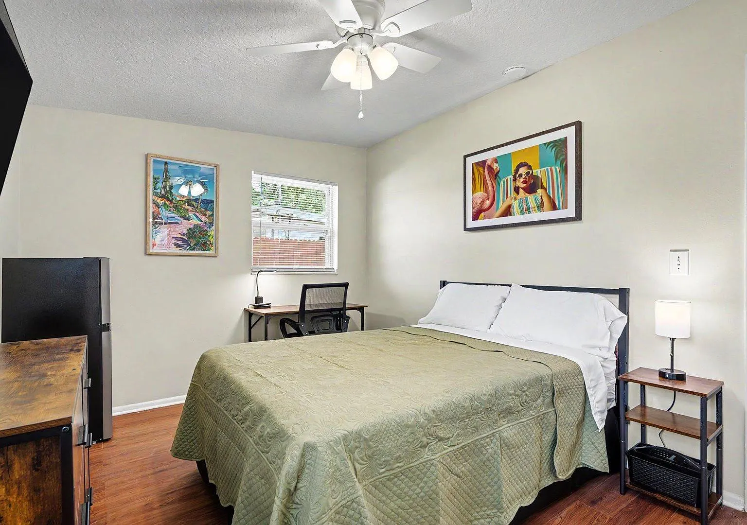 Plenty of space with a full bed, desk workspace, mini fridge, wall-mounted TV, and ceiling fan plus 2 windows for light.