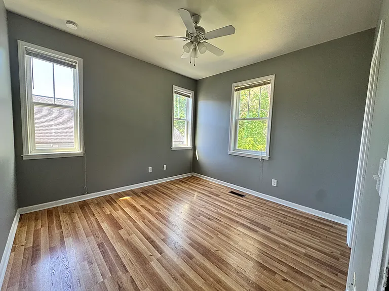 In our first room, you'll find a spacious bedroom with hardwood flooring and natural lighting coming from three windows.