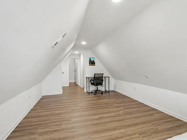 Finished loft-style room with sloped ceilings, durable wood-look flooring, and space for a desk or reading nook.