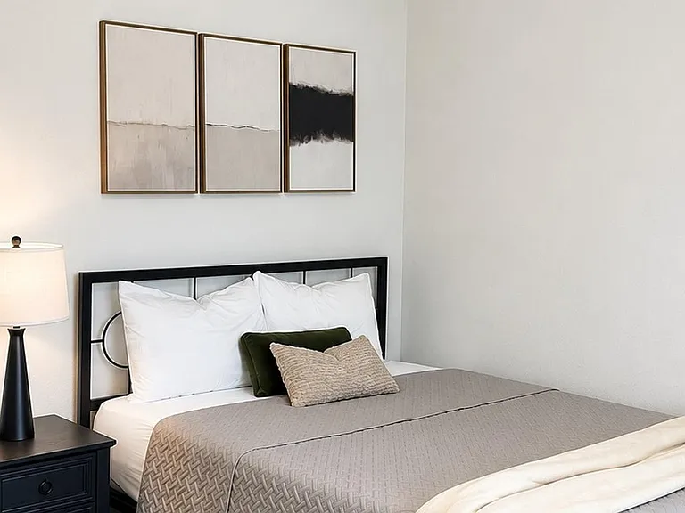 Furnished bedroom with a full-size bed, nightstand and lamp, plus clean wall space for artwork or a desk setup.