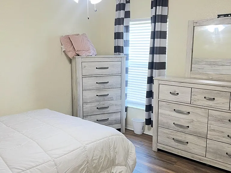 Furnished bedroom featuring a ceiling fan, window with curtains and blinds, and ample storage with a dresser and chest.