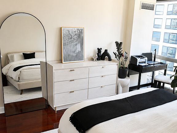 Another angle of the bedroom highlighting crisp walls and dark hardwood floors. The layout offers plenty of room for a full dresser, a large floor mirror, and your office desk setup right by the window without feeling cluttered.