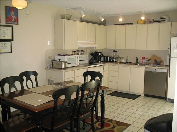 Large tiled kitchen with a newer dishwasher leads to the open dining room, which is also tiled..