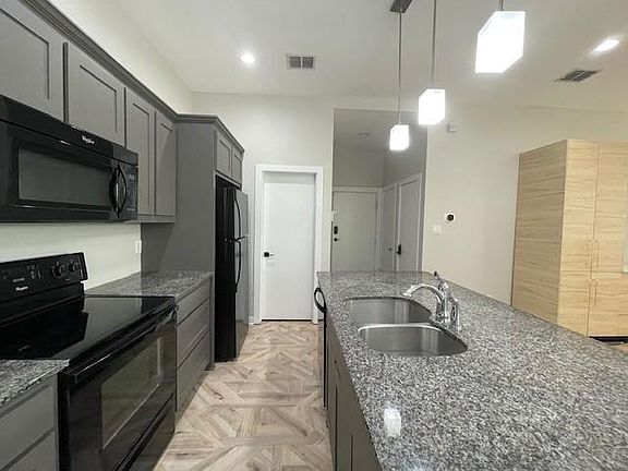 Kitchen featuring black appliances, dark stone counters, hanging light fixtures, and gray cabinets