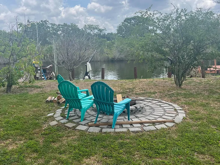 Backyard patio with a circular paver fire pit area, Adirondack seating, and peaceful lake views for outdoor lounging.