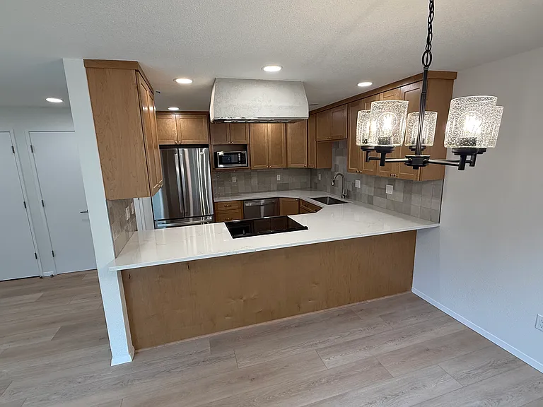 View into kitchen from dining room. New stainless, french door fridge, large stainless steel sink, range with convection oven with an overhead custom Venetian plaster lighted hood.
