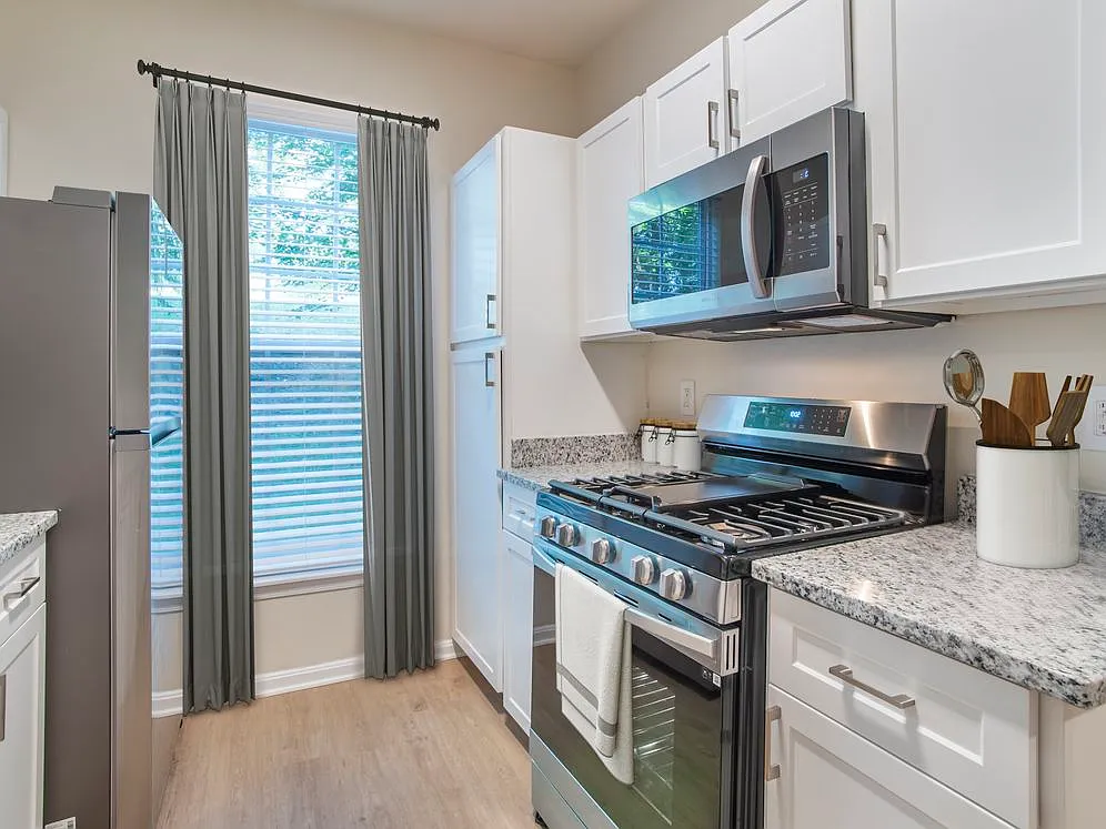 Renovated Package II kitchen with stainless steel appliances, white speckled quartz countertops, white cabinetry, and hard surface flooring - Avalon at Traville