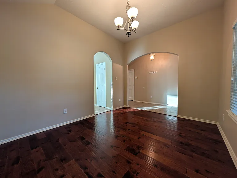 Showcasing the archways leading into the open foyer and kitchen areas, this view highlights the deep-toned hardwood floors and architectural character of the formal dining space.