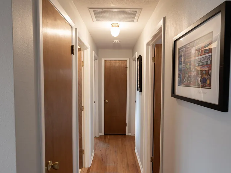 Looking north down the hallway from the dining room to the bedrooms. Left doors are the coat closet, original bathroom, and main bedroom. End of hallway has a linen closet. On the right are two bedrooms.